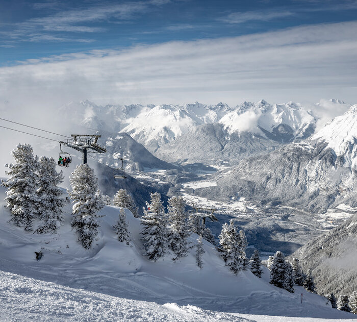 Ein Sessellift umgeben von einer verschneiten Berglandschaft.
