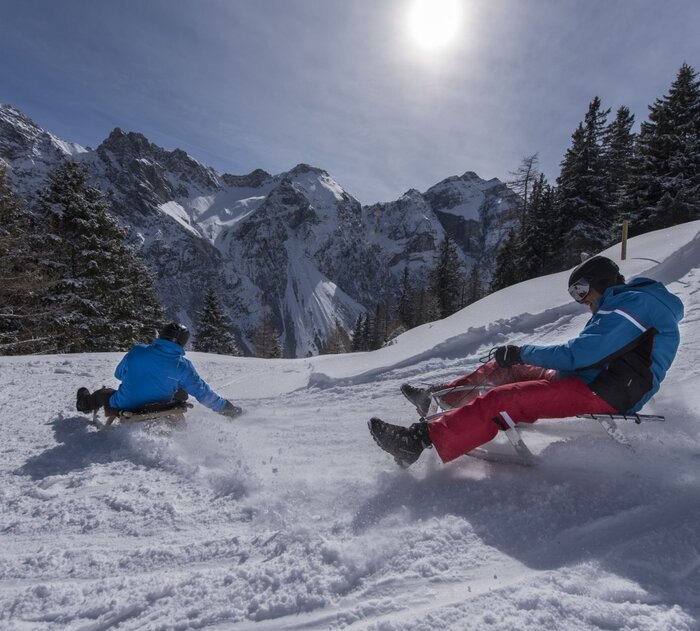 Zwei Rodler rasen eine Piste hinunter.