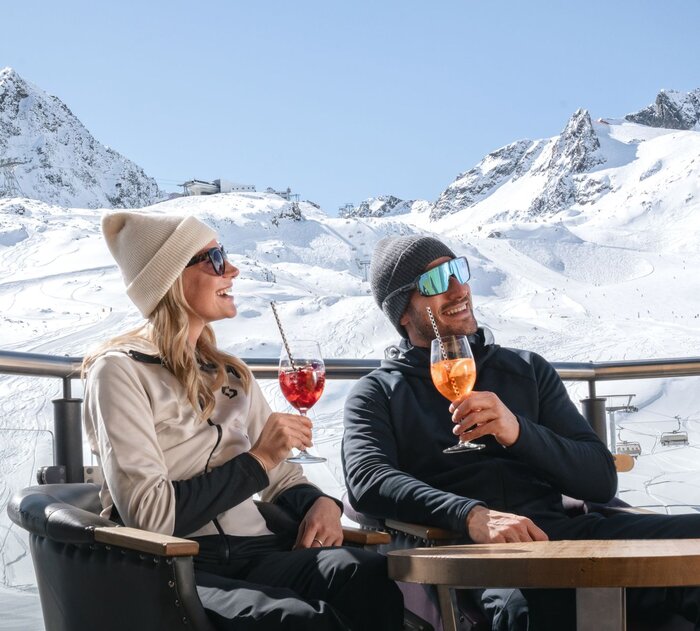 Ein Mann und eine Frau trinken Cocktails vor einer traumhaften Bergkulisse.